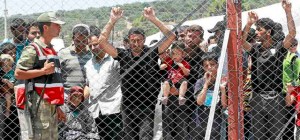 Syrian refugees stand behind the fence of a refugee camp as a Turkish soldier stands guard in the Turkish border town of  Boynuegin in Hatay